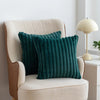A dark teal faux fur stripe decorative throw pillow resting on a cream upholstered armchair.
