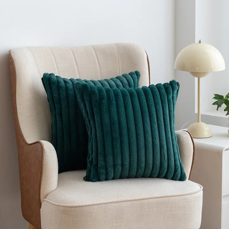 A dark teal faux fur stripe decorative throw pillow resting on a cream upholstered armchair.