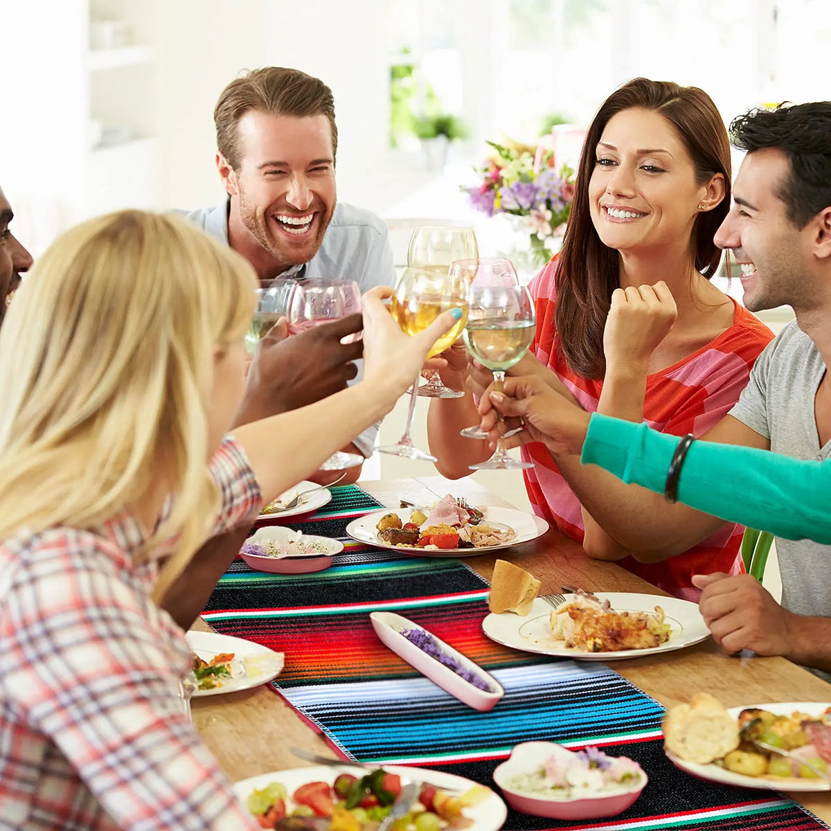 A group of people enjoying a meal together around a table with colorful Mexican Serape table runners.