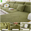 A textured olive green leaf jacquard stretch sofa cover displayed on a sectional sofa with white cushions.