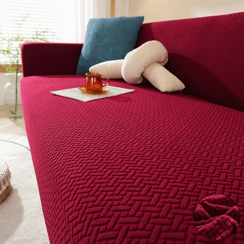 A deep red textured sofa cover with light blue and cream accent pillows and a glass cup on the surface.