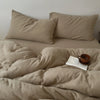 A beige soft 100% cotton duvet cover set with several pillows and a book on a bed.