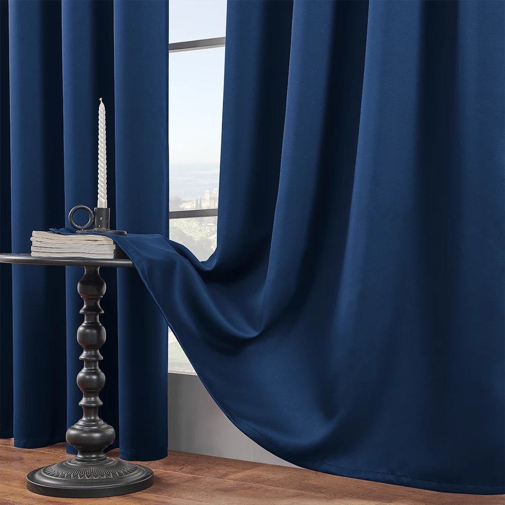 A dark blue blackout window curtain draped next to a table with a candle and stacked books.