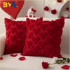 Two red heart-shaped plush cushions resting on a white sofa with scattered red rose petals.
