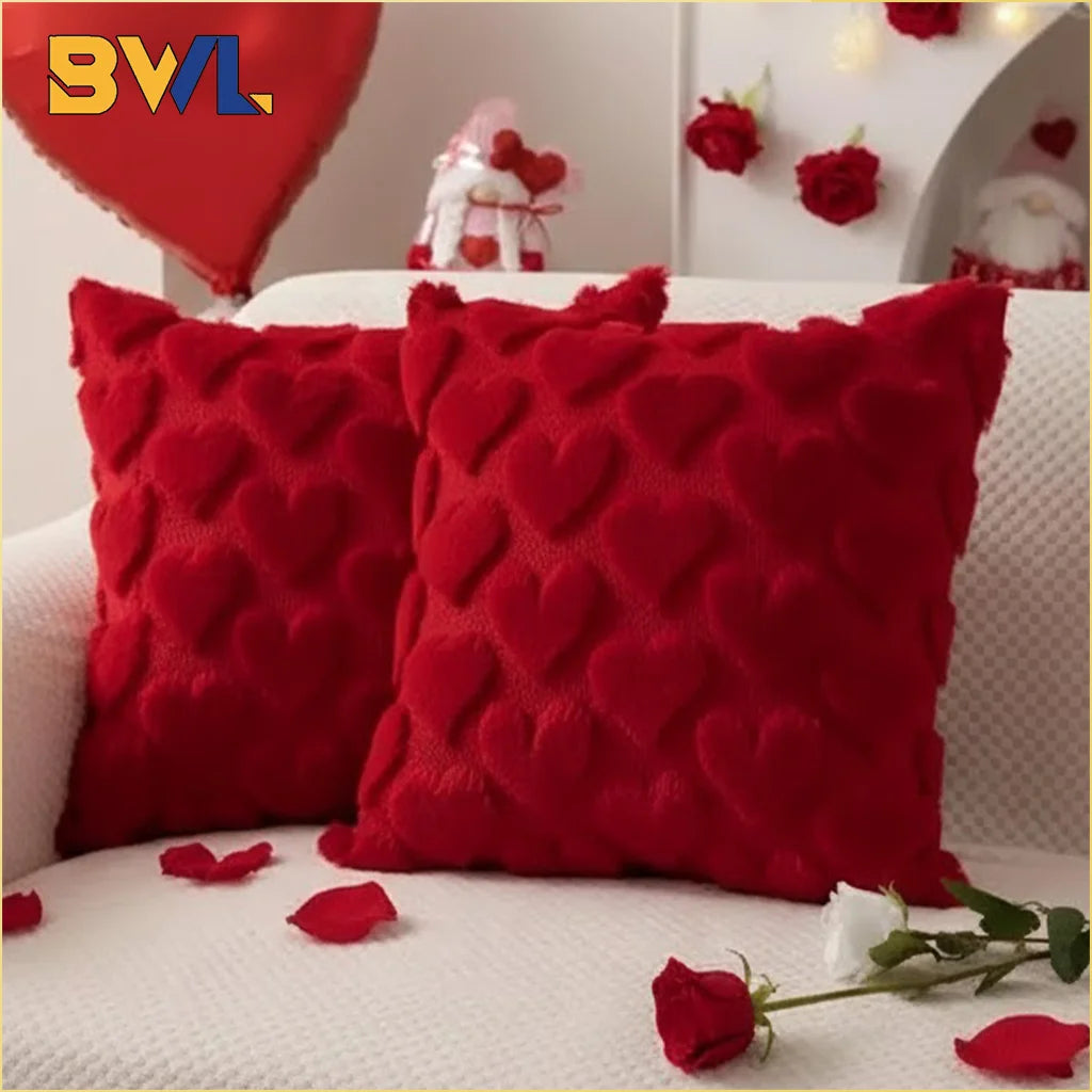 Two red heart-shaped plush cushions resting on a white sofa with scattered red rose petals.