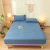 A light blue fitted sheet set on a wooden bed with matching pillows and a bedside lamp.