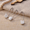 A close-up of stainless steel diaper pins with safety locking closures resting on a beige fabric.