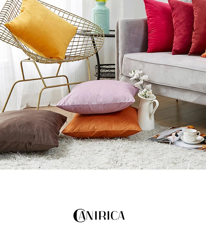 A collection of velvet cushion covers in shades of orange, pink, and red displayed on a light rug.
