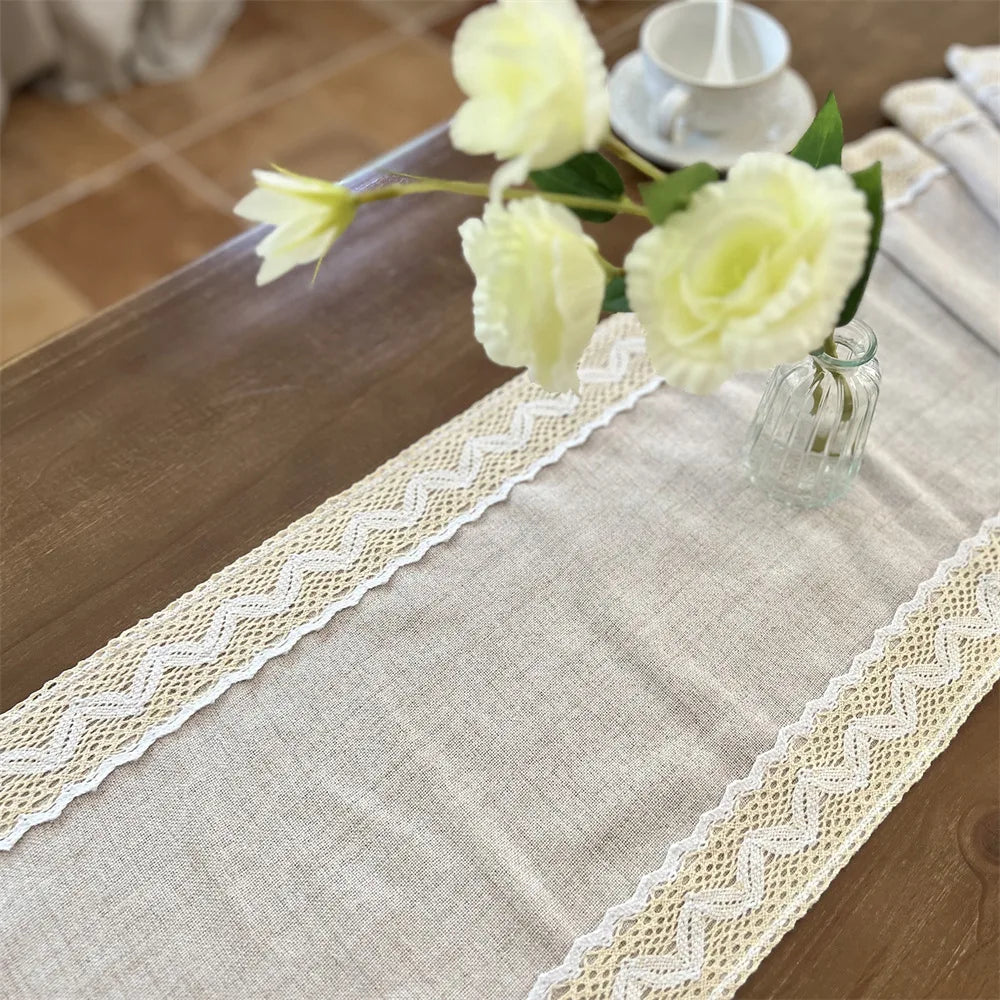 A cream colored crochet macrame lace table runner with yellow roses and a small glass vase.