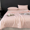A light pink lightweight cooling blanket is displayed on a bed with matching pillows and a candle.