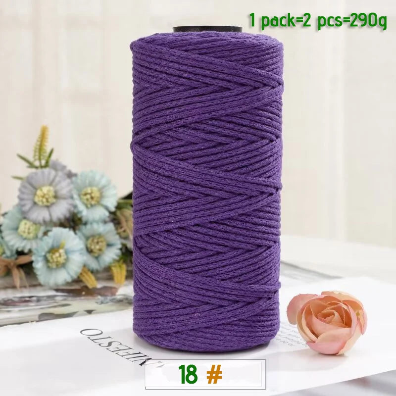 A roll of purple medium-thick hand-woven cotton yarn for crafting, next to a pink rose.