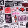 A collection of embroidered patches featuring various phrases and designs on black, pink, and white fabric.