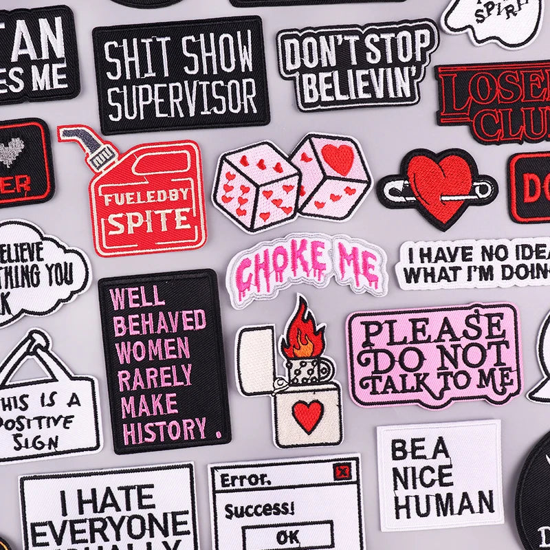A collection of embroidered patches featuring various phrases and designs on black, pink, and white fabric.
