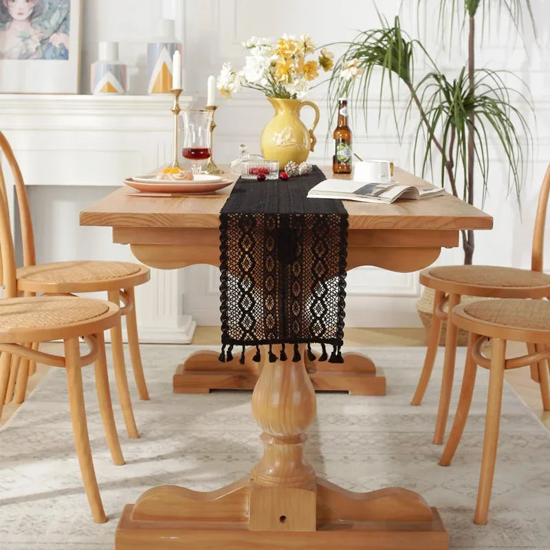 A wooden dining table set for a meal with a black crochet lace table runner and fringe.