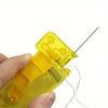 A hand holds a yellow manual automatic needle threader tool with a sharp needle and wire.