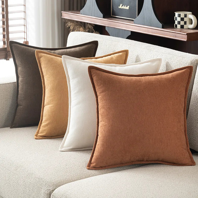 A collection of soft chenille throw pillow covers in shades of brown, gold, and cream arranged on a light-colored sofa.