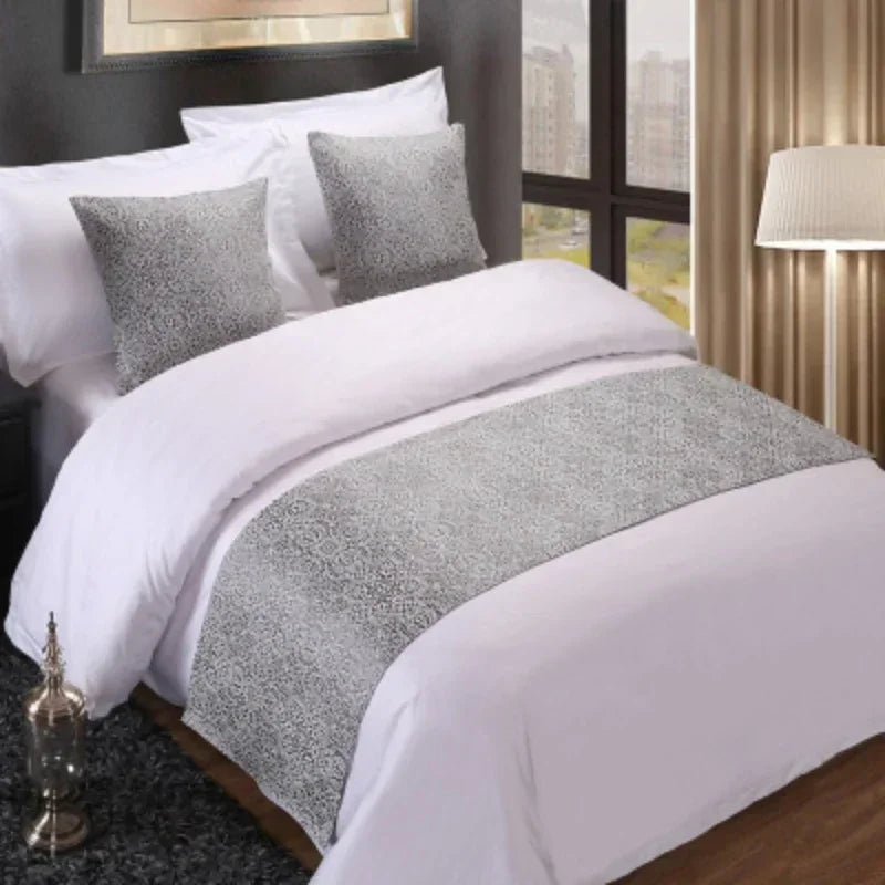 A close-up of a white bed with gray decorative bed flags on the pillows and duvet.
