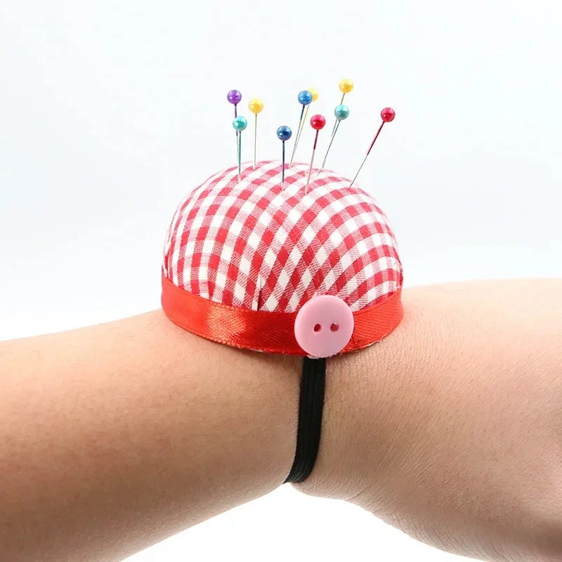 A red and white checkered fabric headpin with colorful pearl-tipped pins attached, worn on a wrist.