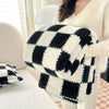A white and black checkered fleece blanket is held by a person in a light sweater.