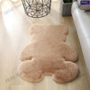 A light brown plush bear-shaped non-slip area rug lying on a wooden floor.