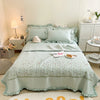 A light mint green floral embroidery quilt bedspread set displayed on a white bed with matching pillows and bedding.
