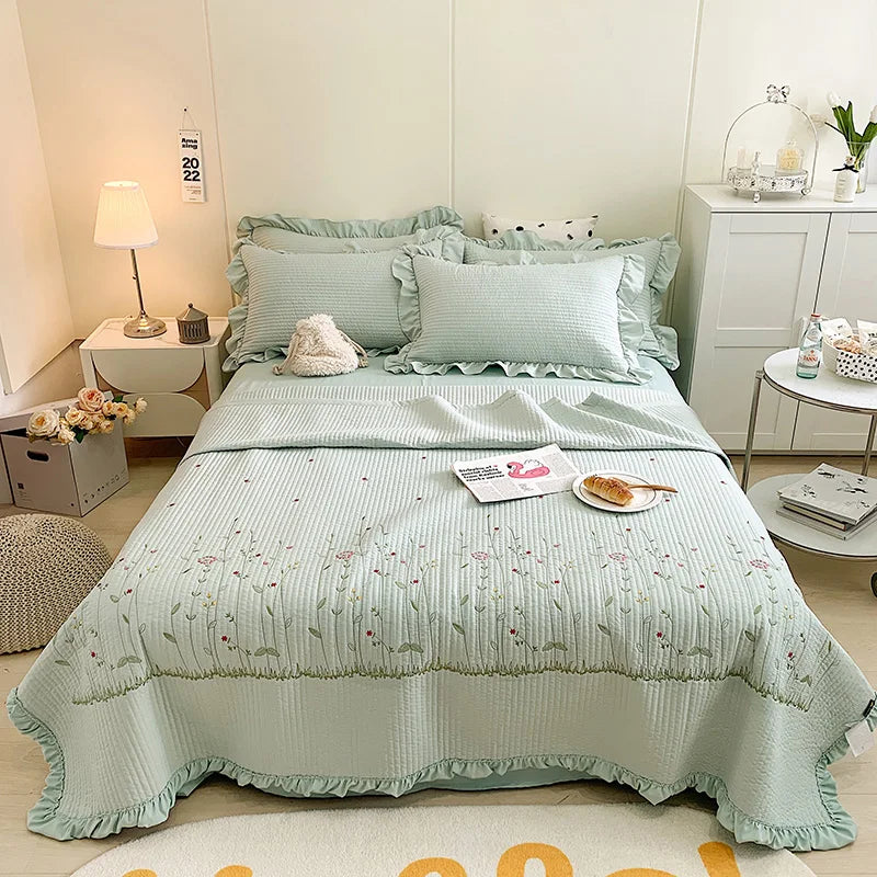 A light mint green floral embroidery quilt bedspread set displayed on a white bed with matching pillows and bedding.