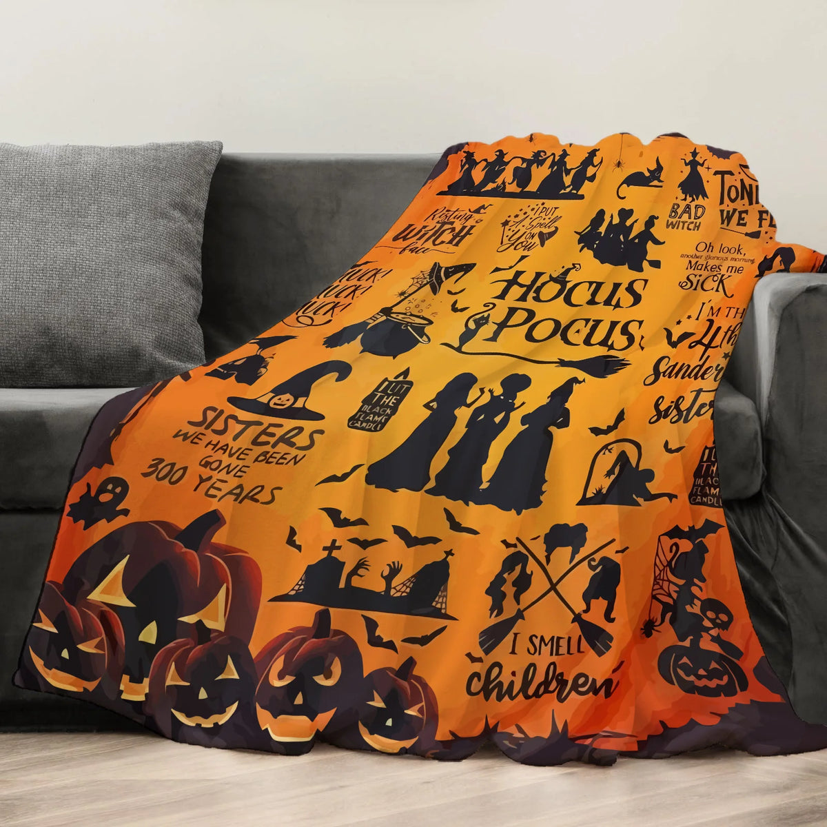 An orange flannel throw blanket featuring Halloween-themed silhouettes and text on a gray sofa.