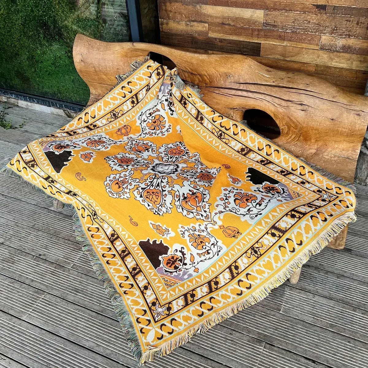 A yellow and white bohemian geometric throw blanket draped over a large wooden log.