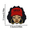 A black and red embroidered patch featuring a woman's face with curly hair and the year 1913 stitched on the forehead.