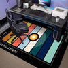 A black gaming desk setup featuring a neon hexagon area rug with colorful stripes and a computer monitor.
