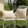 A beige chenille jacquard throw pillowcase with a diamond pattern resting on a woven outdoor chair.