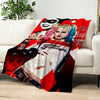 A red and black graphic blanket featuring a stylized woman's face and pink hair on a white sofa.