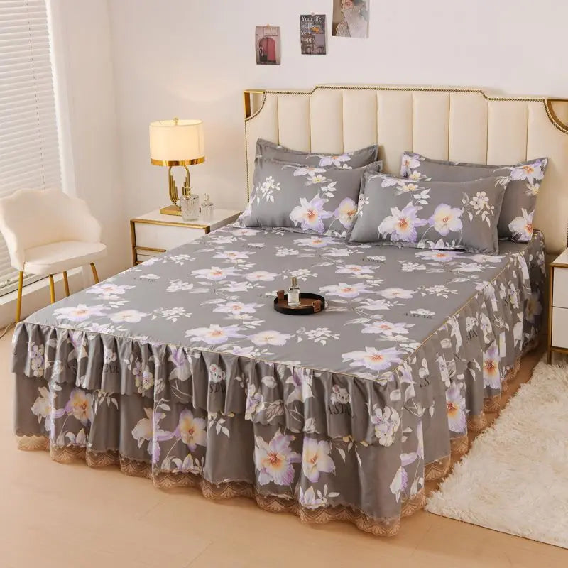 A luxury floral bed skirt in gray and purple flowers covers a bed with a light upholstered headboard.