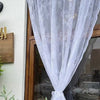 A sheer white curtain with floral embroidery is draped in a window frame.