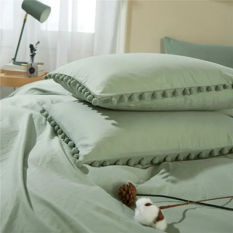 A light sage green duvet cover set with pom-pom trim and a white animal decoration on a bed.