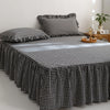 A black and white plaid cotton bed skirt cover draped over a bed.