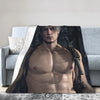 A muscular man with light hair is featured in a dark, dramatic portrait on a throw blanket placed on a sofa.