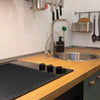 A kitchen countertop showing a heat-resistant silicone stove top cover mat and various cooking utensils.