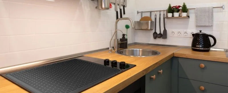 A kitchen countertop showing a heat-resistant silicone stove top cover mat and various cooking utensils.