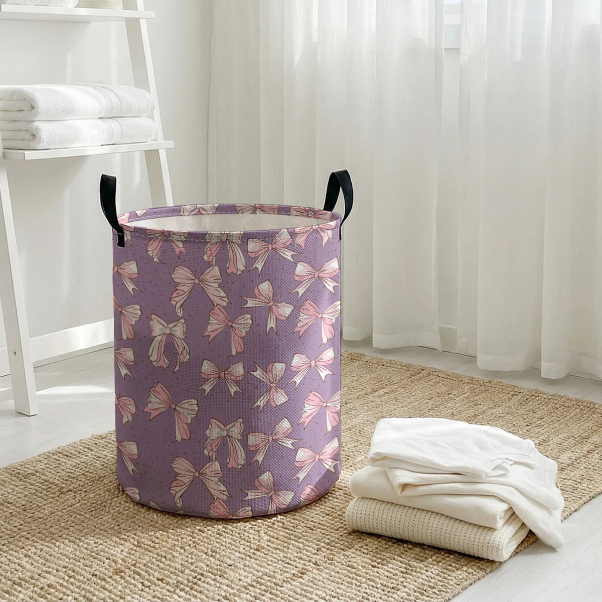 A purple canvas laundry basket with an elegant pink bow pattern sitting on a woven mat.