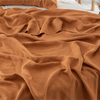 A close-up of a rust orange pure linen flat sheet draped in soft folds on a bed.