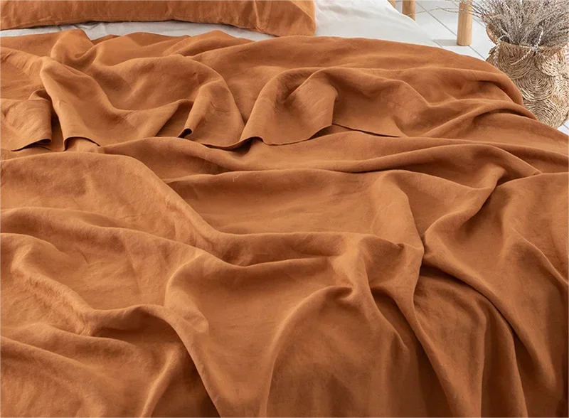 A close-up of a rust orange pure linen flat sheet draped in soft folds on a bed.