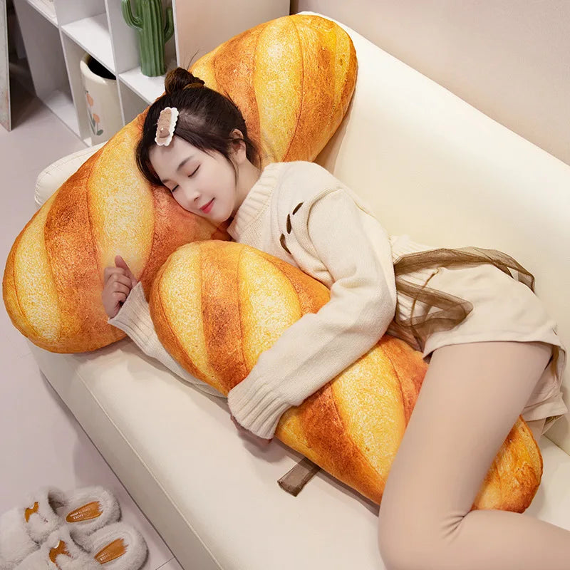 A young woman rests her head on a large, orange striped plush baguette pillow on a white sofa.