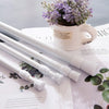 A white adjustable metal curtain rod is shown next to a potted lavender plant on a white surface.