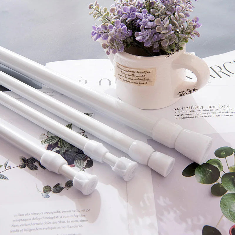 A white adjustable metal curtain rod is shown next to a potted lavender plant on a white surface.