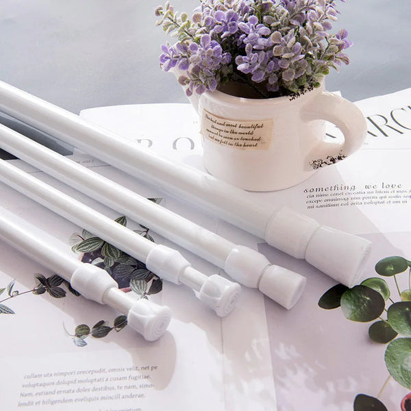 A white adjustable metal curtain rod is shown next to a potted lavender plant on a white surface.