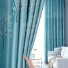 Light blue sheer curtains with a white tree pattern framing a bright window.