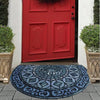 A vintage stone doormat with an intricate blue and white pattern lies on a gray stone step in front of a red door.