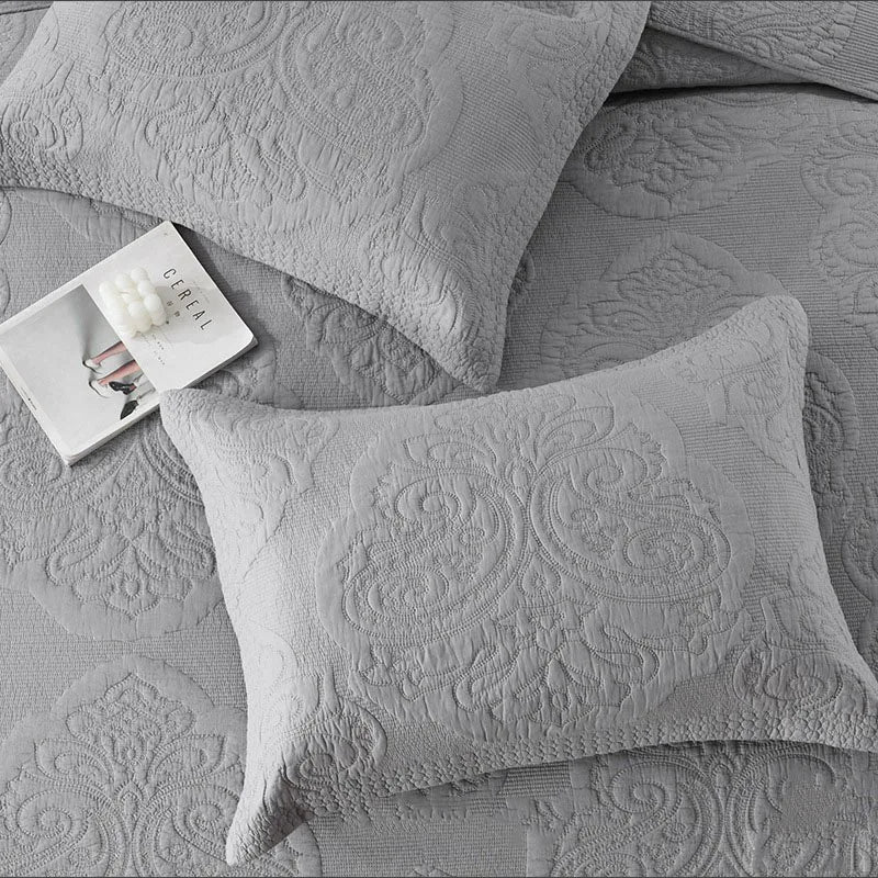 A set of gray embroidered cotton quilted pillow covers with a small white tag.