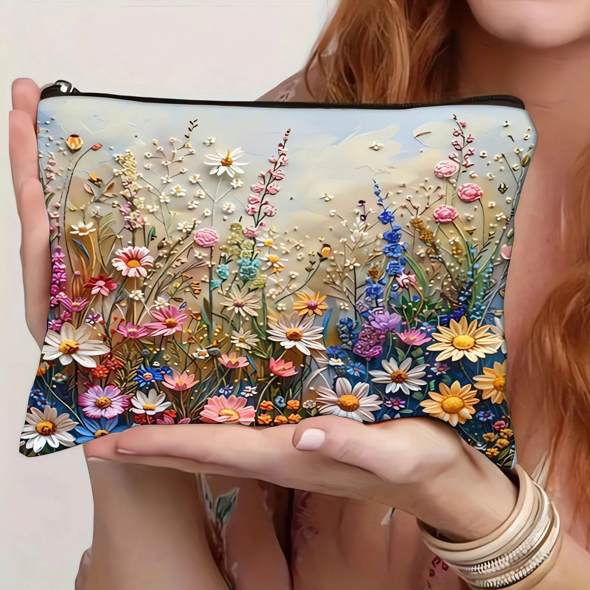 A hand holds a floral canvas cosmetic bag with a zipper closure featuring detailed pressed flowers and greenery.